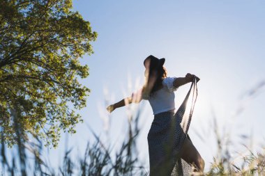 Güneşe karşı buğday tarlasında şapkalı bir kadın.