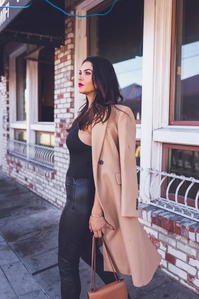 Serious woman walking in front of restaurant with brick walls.