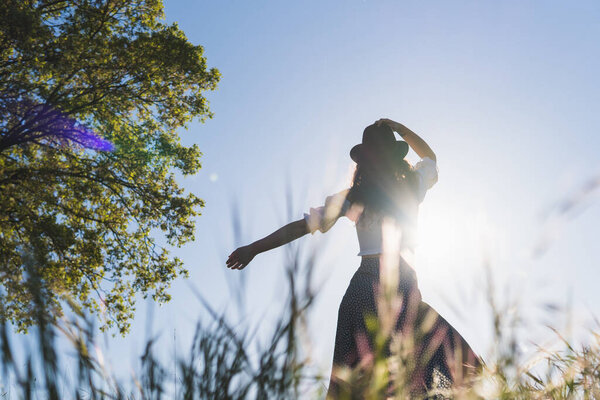 woman with hat in a wheat field against the sun