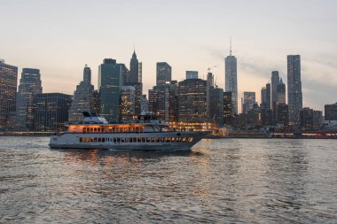 Günbatımında New York 'ta gökdelenlerin yakınında dalgalı denizde yüzen beyaz yolcu gemisi bulutsuz gökyüzünün altında.