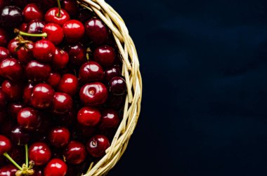 Koyu arkaplanda bir bardakta olgun kiraz, boş bir alan.