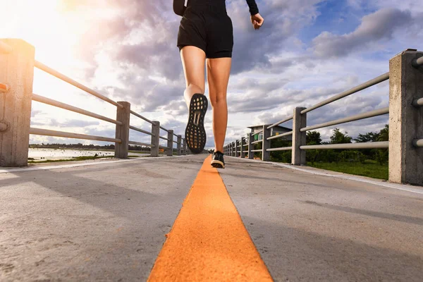 Legs of the woman running on city bridge road.Sporty woman running on road at sunrise. Fitness and workout wellness concept.