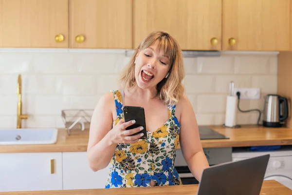 Surprised Woman Looking Her Phone Laptop Kitchen Table — Stock Fotó