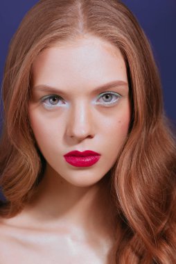Young woman with long red wavy hair, green eyeshadows, red lipstick.