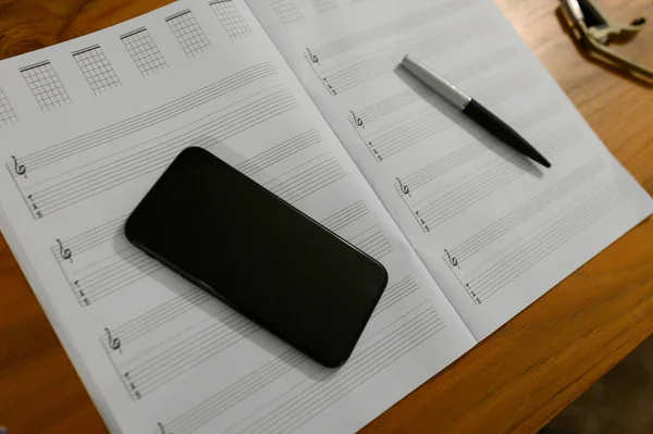 Side view of blank music staff, guitar tab and phone on desk
