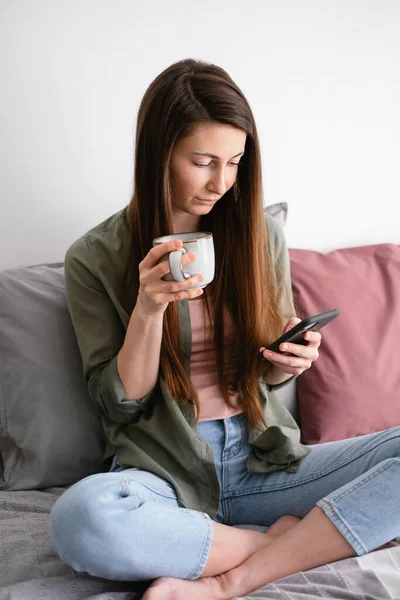 Young Woman Sitting Bed Cup Tea Using Smartphone — Stok fotoğraf