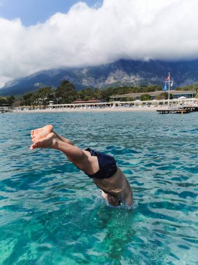 Şort giyen bir adam platformdan denize atlıyor.