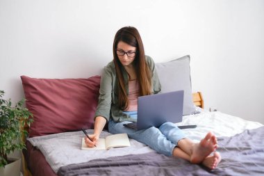 Konsantre genç kadın serbest çalışan notlar alıyor. Evden çalış..