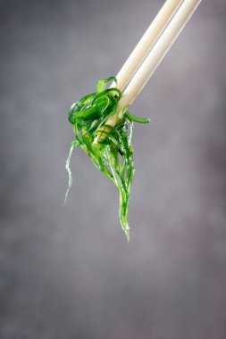 Tahta çubuklarla tutulmuş Wakame salatası.