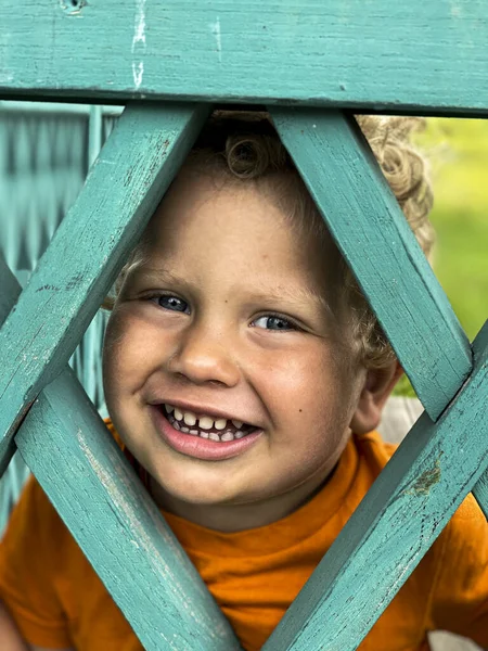 2岁的男孩从绿色篱笆上的孔里往外看 — 图库照片