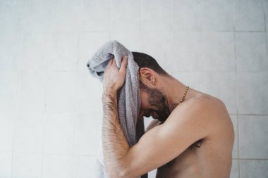 Beyaz adam banyoda kendini kurutuyor.
