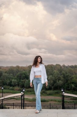 Kot pantolonlu, beyaz bluzlu, bulutlu bir kadın..