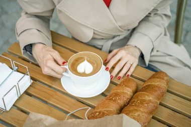 Elleri bir fincan kahve ve ekmeği ahşap bir masada tutuyordu..