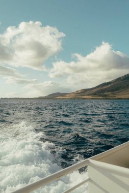 Sunlit ocean wake off the coast of Maui under cloudy sky