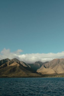 Golden Maui mountains with cloud cover above deep blue ocean