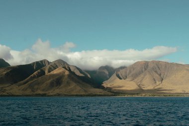 Golden Maui mountains with cloud cover above deep blue ocean