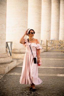 Çizgili elbiseli bir kadın eski sütunların yanında yürüyor.