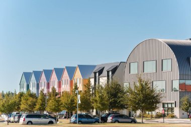 Renkli modern evler ve açık mavi gökyüzünün altında park edilmiş arabalar..