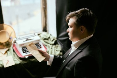 Resmi kıyafetli bir adam klasik bir daktilonun yanındaki mektubu okuyor.