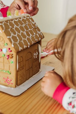 Ebeveyn ve çocuğun zencefilli kurabiye evini birlikte dekore etmesini kapatın.