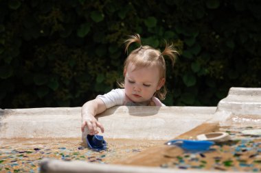 At kuyruklu şirin kız güneşli bir günde oyuncak tekneyle oynuyor.