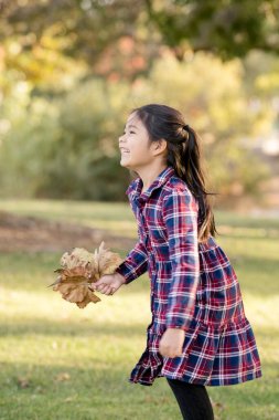 Gülümseyen kız güz gününde yapraklarla koşar