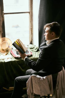 Klasik bir ayarda pencerenin yanında kitap okuyan kişi