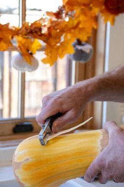 Man peeling butternut squash at a kitchen window