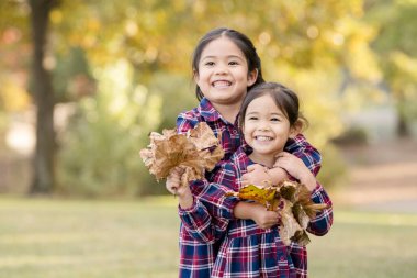 Kucaklayan kız kardeşler büyük gülümsemeli yapraklar tutuyorlar.