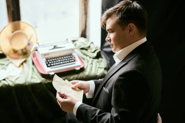 Takım elbiseli bir adam eski bir daktiloyla mektup okuyor.