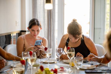 Masada oturup resim yapan ve akıllı telefon kullanan kadınlar.