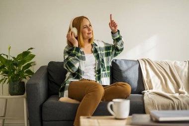 Kanepede oturan ve kulaklıkla müzik dinleyen bir kadın.