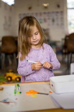 Küçük kız içeride bir zanaat aktivitesi yapıyor, sanat projesi yaratıyor.