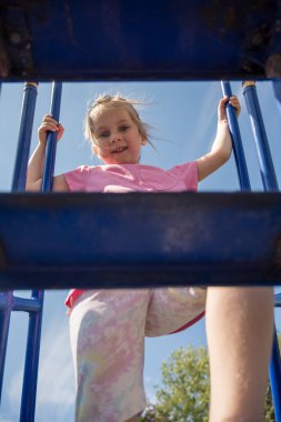 Küçük kız oyun alanında oynuyor, kaydırağın merdivenlerini tırmanıyor.