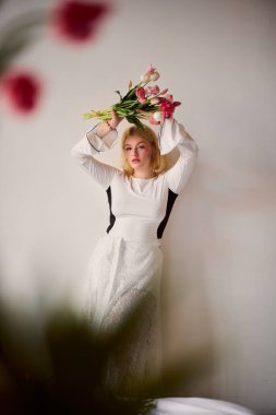 Çiçekleri olan genç bir kadın zarif bir şekilde poz veriyor.