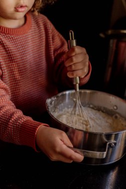 Mutfak tezgahında metal kasede hamuru çırpan çocuk.