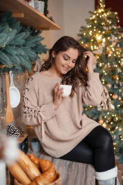 Esmer kadın kahve içiyor ve mutfakta oturuyor.