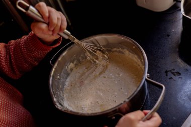Mutfak tezgahında metal kasede hamuru çırpan çocuk.