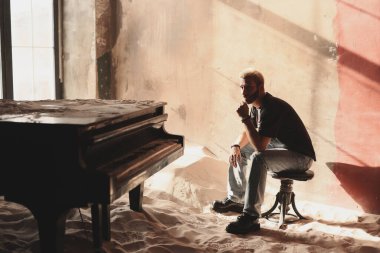 Müzisyen, sanatsal bir ortamda piyanonun başında düşünceli bir şekilde oturur.