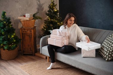 Noel ağacının yanındaki kanepede oturan bayan hediyeleri inceliyor.