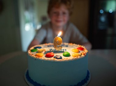 Genç çocuk doğum gününü renkli bir pasta ve sıcak bir gülümsemeyle kutluyor.