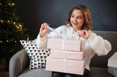 Kanepede otururken hediye kutusuna fiyonk bağlayan neşeli genç bayan.