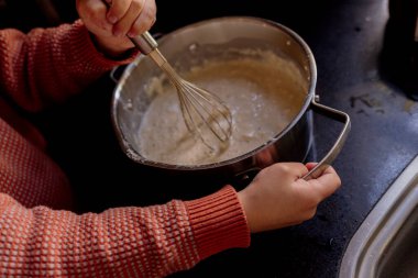 Mutfak tezgahında metal kasede hamuru çırpan çocuk.