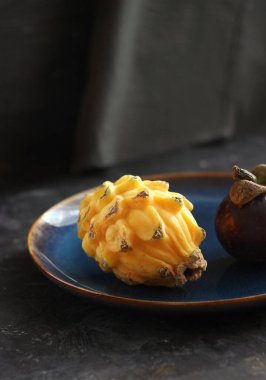 Sarı pitaya ve mangosteen masada bir tabakta yatıyor.