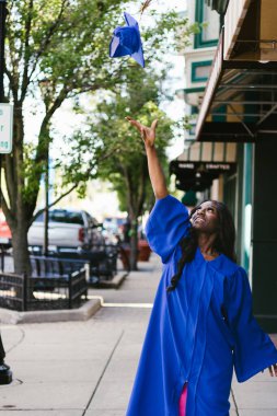 Mutlu mezunlar, kentsel alanda önlük giyerek şapka takıyor.