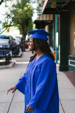 Mutlu siyah kadın mezuniyet için kep ve cübbe içinde güler.