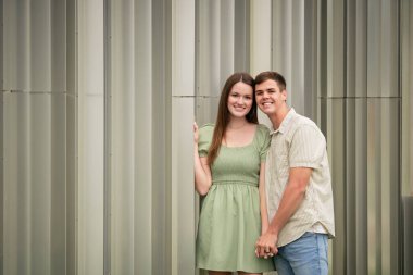 Gülümseyen çift metal duvarın önünde birlikte poz veriyor.