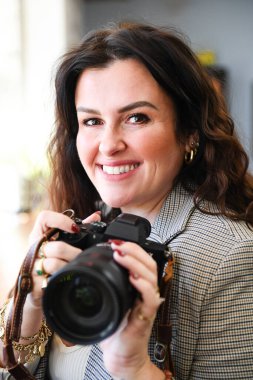 Gülümseyen kadın, elinde altın mücevherlerle ceketinin içinde kamera tutuyor.