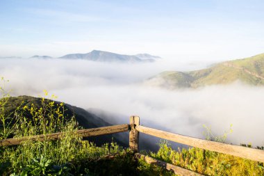 Sabahın erken saatlerinde sisli dağ vadisine bakan ahşap çitler.