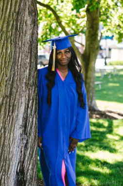 Mezuniyet kepi ve cübbesi içinde güzel mutlu siyah kadın.